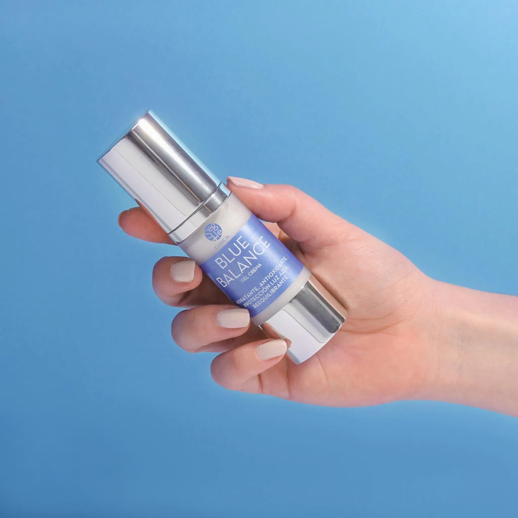 foto de una mano sosteniendo el producto de crema antibrillos y crema matificante blue balance con fondo azul haciendo alegorí